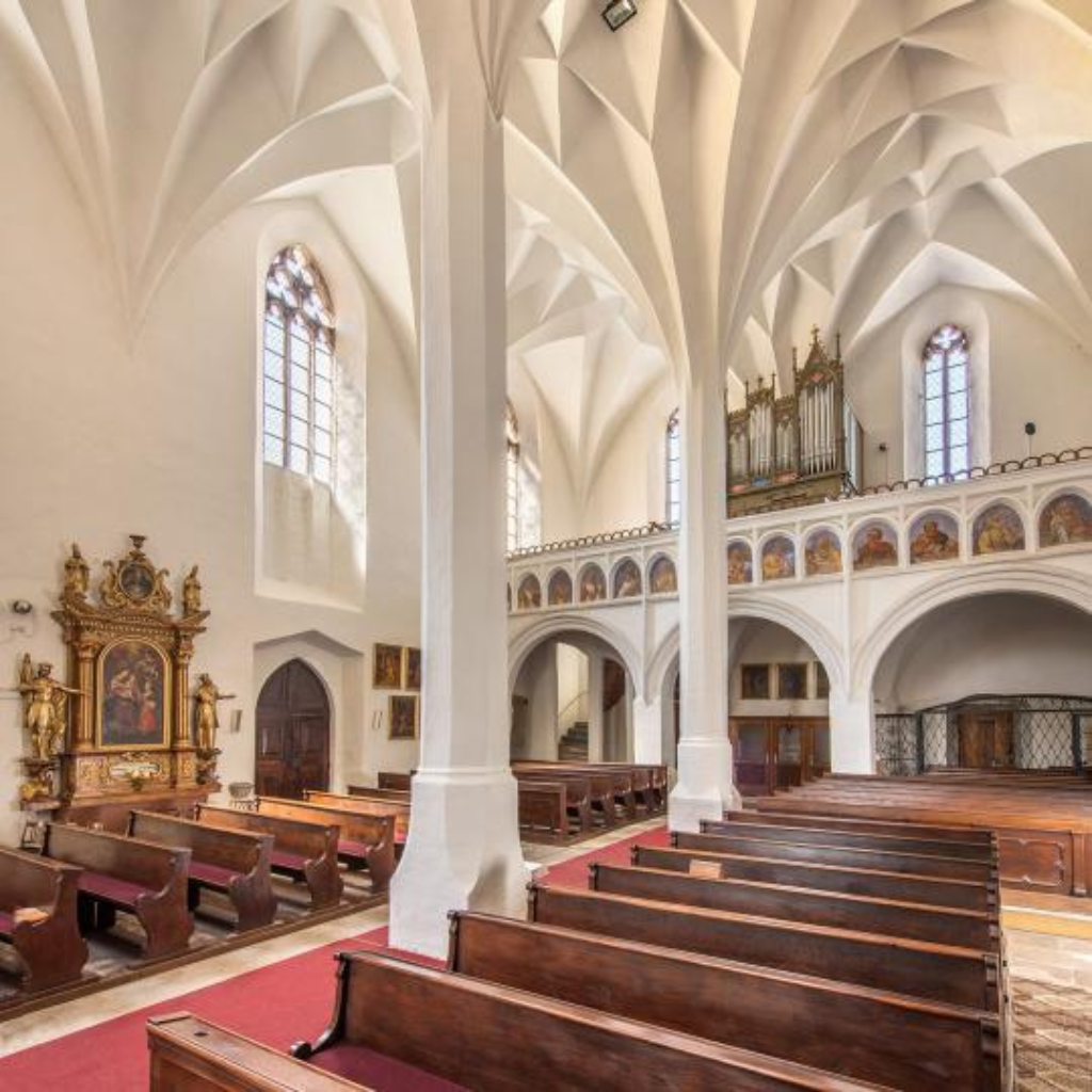 Pohled zevnitř kostela sv. Petra a Pavla na zdobenou klenbu směrem ke kazatelně, s detaily architektury a teplým osvětlením.