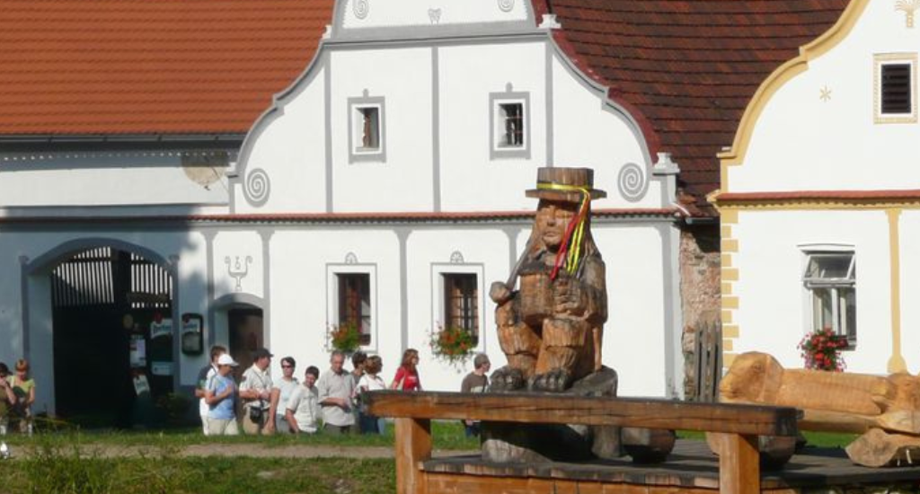 Malebný jihočeský barokní dům s vodníkem sedícím u rybníka v poklidné krajině.